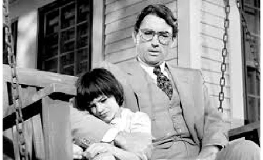 Black and white still of Atticus Finch seated on a porch with his daughter, from the film To Kill a Mockingbird