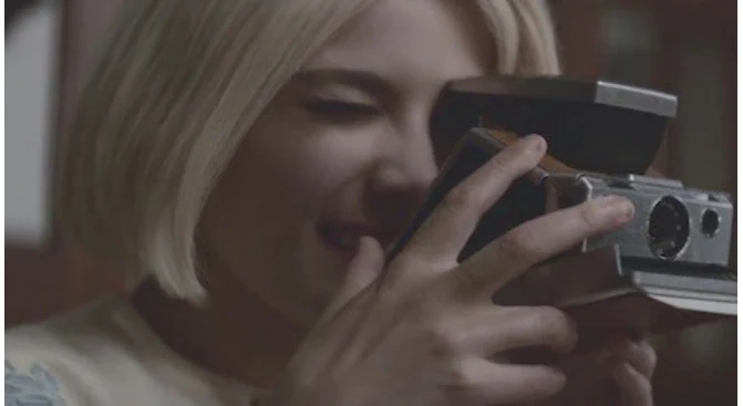 A woman holding an instant camera, from the video for Colors